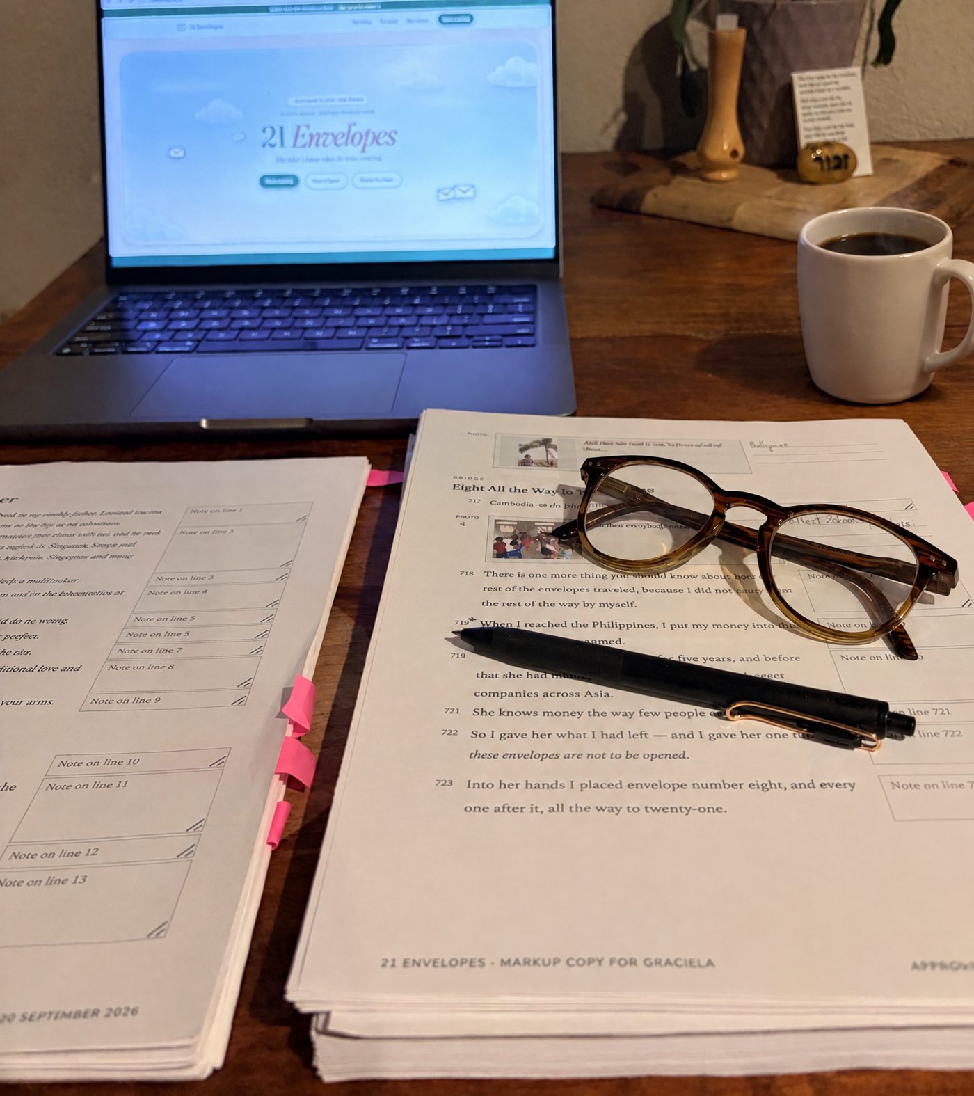 Jenny's desk: a marked-up manuscript of 21 Envelopes, her glasses and pen, a cup of coffee, and the book's website on the laptop